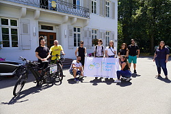 Von links nach rechts stehen Angelo Coutinho, Harald Kleem, Chuck Niessit, Mirways Saberi besuchen auf ihrer Climate Cycle Tour die jugendlichen Vertreter  Eduard Metzler, Alina Treiber, Oliwia Stollorz,  Darin Aslan und Taner Demiralay vom Kinder- und Jugendzentrum Schlachthof und Klimaschutzmanagerin Madeleine Krol. Sie halten ein weißes Banner mit der Aufschrift "Climate Cycle Tour" und stehen vor dem Rathaus 1.