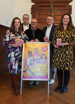 Von Links Valerie Silberer, Abteilungsleiterin Kultur, Guido Schöneboom, Lahrs Erster Bürgermeister, Tobias Meinen, Leiter des Amts für Kultur, Musik und Medien, Dieter Leidinger, Volksbank Lahr und Yvonne Berndt, Presse- und Öffentlichkeitsarbeit und Kulturmarketing. Mittig steht ein Plakat mit dem neuen Design für das Abo Programm. Das Plakat sticht durch ein orange pink farbenes Design hervor.