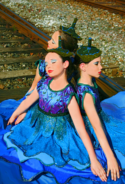 Drei Mädchen in blauen Glitzer-Kleidchen sitzen im Kreis, Rücken an Rücken und haben die Augen geschlossen.