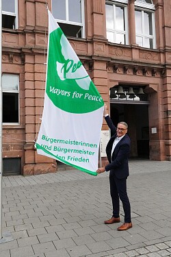Oberbürgermeister Markus Ibert hisst die Flagge der „Mayors for Peace“ am Rathaus Luisenschule.