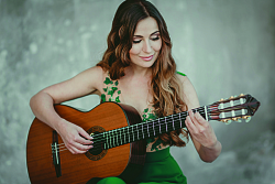 Gitarristin Yulia mit braunem, gewelltem Haar sitzend in grünem Kleid spielt eine Konzert-Gitarre.