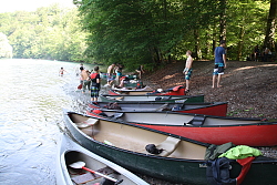 Das Bild zeigt Jugendliche, die gerade das letzte einer ganzen Reihe von Kanus ans Flussufer ziehen. Einige Jugendliche stehen dabei im Wasser, einer sogar bis zum Bauch.