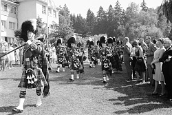 Parade mit einer Band mit Pipes und Drums, mit Fellmützen und im Schottenlook in schwarz-weiß. 