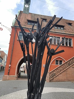 Reinhard Sigles Werk &#34;Hilfe&#34; befindet sich auf dem Urteilsplatz. Das Werk besteht aus mehreren schwarzen Brettern, die in die Form von Personen angebracht wurden, die die Arme in die Luft srecken.