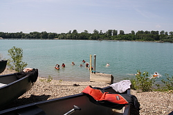 Das Bild zeigt über zwei Kanu-Spitzen hinweg eine Gruppe von Mädchen, die im Baggersee badet. 