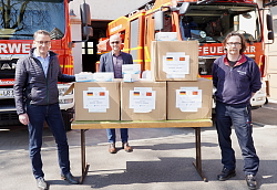  Schutzmasken aus China - die Masken stehen auf einem Biertisch in Kartons verpackt. Dahinter parken zwei Feuerwehrautos. Von links um die Masken mit ausreichend Sicherheitsabstand stehen Oberbürgermeister Markus Ibert, Arnfried Sickinger, Leiter des Büros des Oberbürgermeisters, und Thomas Happersberger, Kommandant Feuerwehr Stadt Lahr. 
