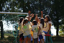 Das Bild zeigt ein Gruppe Mädchen in selbstgemachten Sportleibchen, die sich vor einem Tor abklatschen.