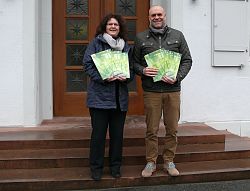 Die Leiterin der Volkshochschule Lahr, Carmen Wenkert, und der Leiter des Amts für Außerschulische Bildung, Tobias Meinen, stehen vor dem Rathaus 1 in Lahr und halten die neuen VHS Programmhefte in den Händen. 
