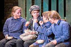 Das Bild zeigt Oliver Twist, der zwischen drei anderen Straßenkindern sitzt, die ihm die Faust zeigen.