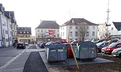 Das Bild zeigt einen Blick auf den neuen Altglascontainer-Standort an der Friedhofstraße Lahr. Von links nach rechts sind Häuser, die Friedrichstraße, ein Fußgängerweg, Stellplätze und der Parkplatz eines Lebensmitteldiscounters mit Autos zusehen. Die zwei Altglascontainer stehen auf dem vorderen der Stellplätze zwischen Fußgängerweg und Parkplatz.