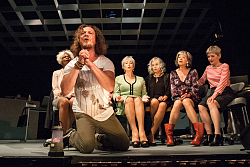 Das Bild zeigt einen Mann, der mit flehendem Blick und zum Gebet gefalteten Händen vor den Sekretärinnen kniet.