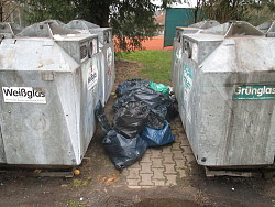 Das Bild zeigt Müllsäcke zwischen zwei Altglascontainern