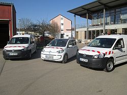 Das Bild zeigt die drei neuen Fahrzeuge des BGL, Links und rechts je einen weißen VW Caddy und in der Mitte das weiße Elektroauto VW UP E-UP HIGH.