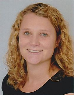 Das Bild zeigt ein Porträt von Annika Martini. Sie hat blondes, schulterlanges, gelocktes Haar und trägt ein dunkles T-Shirt.