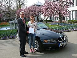 OB Dr Müller gratuliert Sophie Fromknecht vor ihrem Auto mit dem 22 222sten LR-Kennzeichen und überreicht ihr den Gutschein für eine Jahreskarte zur Landesgartenschau 2018 in Lahr. Das Auto steht im Innenhof des Rathaus 1. Im Hintergrund sieht man den frühlingshaften Park mit blühenden Kirschbäumen.