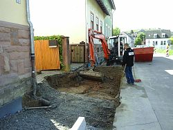 Vor zwei Hofeinfahrten in der Bottenbrunnenstraße reißen Bauarbeiter mit Bagger die Straße auf. Die Baustelle ist abgesperrt und es steht ein Container auf der Straße.
