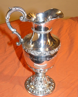 Auf dem Bild sieht man einen großen silbernen Taufkrug. Darauf steht: gestiftet von CM Jamm