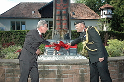 Oberbürgermeister Dr. Wolfgang G. Müller und Oberst i.G. Tom Endicott enthüllen eine Gedenktafel am Totempfahl im Stadtpark. Beide ziehen an unterschiedlichen Enden einer roten Schlaufe. 