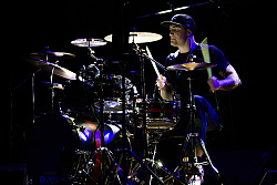 Die Städtische Musikschule veranstaltet wieder Magic Drums. Das Bild zeig einen Schlagzeuger mit Basecap wirbelnd am kombinierten Schlagzeug. Der Hintergrund ist schwarz. Der Musiker wird lediglich von blauen Lichteffekten ins Licht gesetzt. 