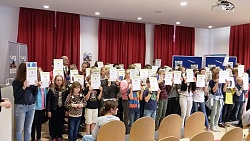 Viele Kinder stehen auf der Bühne und halten jeweils eine Urkunde vors Gesicht und in die Kamera.