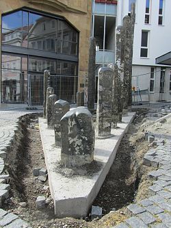 Das Bild zeigt die Basalt-Stelen noch im Rohbau in neuer Anordnung, das Fundament hat eine dreieckige Form. Sie stehen direkt vor dem ehemaligen Menzer-Gebäude in der Kaiserstraße. 