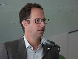 Bei der Einweihungsfeier des Erweiterungsbaus der Otto-Hahn-Realschule Lahr sprach der Architekt. Er steht am Mikro mit Jacket, weißem Hemd und Brille.  