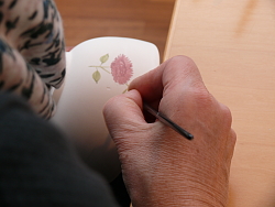Neues Souvenir der Chrysanthema Lahr.
Eine Kerammalerin bemalt ein weißes Schälchen mit altrose Chrysanthemen. Das Bild zeigt den genauen Pinselstrich. 