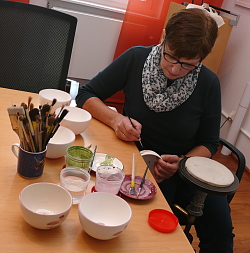 Neues Souvenie der Chrysanthema Lahr.
Eine Kerammalerin bemalt ein weißes Schälchen mit altrose Chrysanthemen. 