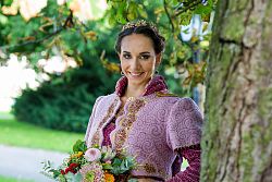 Das Bild zeigt Chrysanthemenkönigin Lea Johanna I. Sie steht mit einem bunten Blumenstrauß in den Händen nah an einem Baum, der Hintergrund im Bild ist verschwommen.