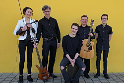 Die fünfköpfige Bande FES-Tones, bestehend aus vier männlichen Mitgliedern und einer jungen Frau. Alle stehen vor einer gelben Wand. Die Herren tragen alle schwarze Hemeden bzw. Shirts, die Frau ein weißes Jacket mit schwar-weiß gestreiftem Shirt und schwarzen Hose. Sie hält eine Geige in der Hand, der Mann neben ihr eine E-Gitarre und ein weiterer eine Akustik-Gitarre.