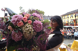 Zu sehen ist Floristin Gudrun Kruss mit einem üppigen Blumenstrauß mit großen Chrysanthemen bei einer Vorführung auf der Marktplatzbühne. Im Hintergrund das Publikum auf Bänken sitzend.