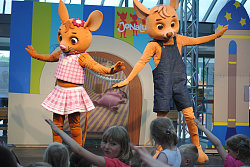 Das aus dem Kinderfernsehen bekannte Trio „JoNaLu“ bei einem Auftritt. Zu sehen sind zwei lebensgroße Figuren in einem Mauskostüm, ein Mäuse-Junge und ein Mäuse-Mädchen. Beide stehen tanzend auf einer Bühne vor der Kinder stehen.