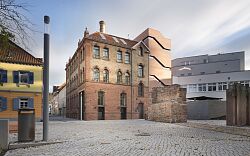 Man sieht ein Gebäude aus Ziegeln, die ehemalige Tonofenfabrik, in der sich ein Teil des stadtgeschichtlichen Museum wiederfindet.
Es hat 3 Stockwerke, hohe Fenster und einen ebenso hohen Anbau rechter Hand aus rosafarbenem Beton.