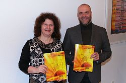 Die Stadt Lahr stellt das neue Programm der Volkshochschule Lahr vor.
Auf dem Bild stehen Carmen Wenkert (VHS-Leiterin) und Tobias Meinen (Leiter Amt für außerschulische Bildung) nebeneinander. Jeder hält ein orangerotes VHS-Programm vor die Brust und lächelt in die Kamera. 