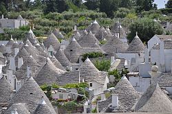 Foto von Hausdächern, die alle kegelförmig nach oben in einer Spitze zulaufen und mit grauen Ziegeln eingedeckt sind. Vereinzelt sind weiße Schornsteine und Mauern zwischen den Dächern zu sehen.