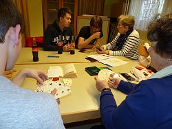 Helga Brunner erklärt im Vordergrund Jakob Schwerer die Spielregeln von Canasta während Ursula Hildenbrand Nachhilfe von Luca Munzig und Ricco Herrmann an ihrem Smartphone bekommt.