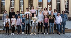 Die erfolgreichen Musikschüler haben sich teils mit Instrument im Hof des ehemaligen Scheffels vor einem Baum platziert. Im Hintergrund die alte Turnhalle, der heutige Konzertsaal.