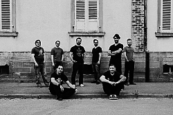 Bild der Gruppe NoAuthority in schwarz weiß. sitzen vor einem älteren Gebäude in schwarzer Kleidung ohne Instrumente.