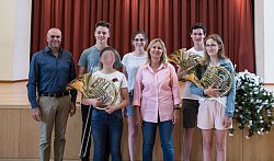 Erfolgreiche Musikschüler präsentieren sich mit Ihren Instrumenten in einem Gruppenbild vor der Bühne des Konzertsaals &#34;Altes Scheffel&#34; und lächeln in die Kamera. 