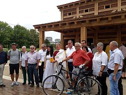 Mehrere Personen stehen anlässlich der Eröffnung des Römer-Radwegs für ein Pressefoto vor der Nachbildung des römischen Streifenhauses auf dem Landesgartenschaugelände in Lahr, darunter auch Oberbürgermeister Dr. Müller, der ein römisches Gewand trägt. Neben ihm steht eine Dame, ebenfalls römisch gekleidet. Alle anderen tragen Freizeitkleidung, teilweise haben sie Rucksäcke dabei. Ein Herr im karrierten Freizeithemd hält ein Fahrrad.