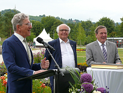 OB Dr. Müller steht am Mikro und bedankt sich. Daneben stehen Altkanzler Schröder und Martin Herrenknecht. Im Hintergrund ist der Schutterlindenberg zu sehen. 