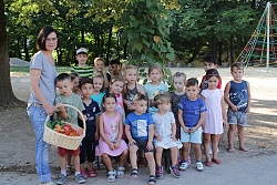 Gruppe mit etwas 20 Kindergartenkindern und ihrer Erzieherin haben sich mit einem Korb voll Obst und Gemüse zum Gruppenbild aufgestellt.