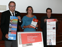 Hinter einem Aufsteller mit dem Deckblatt des Spielzeitmagazins stehen EBM Guido Schöneboom, Yvonne Berndt und Gottfried Berger von links nach rechts und halten jeweils ein Plakat oder Flyer in den Händen.
