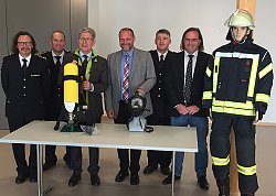 Das Bild zeigt von links Thomas Happersberger, Bernd Leppert, Dr. Wolfgang G. Müller, Wolfgang Brucker, Achim Zehnle und Carsten Gabbert. Neben den Herren steht eine lebensgroße Puppe in eine Feuerwehrausrüstung. Vor ihnen befinden sich auf einem Tisch eine Sauerstoffflasche und eine Atemschutzmaske wie sie in den Einsätzen von den Einsatzkräften benutzt werden.