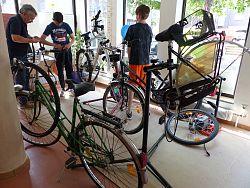 Blick in die Fahrradwerkstatt des Repair-Cafés. Mehrere Fahrräder stehen dort und dazwischen zwei Jugendliche und ein Reperateur. 