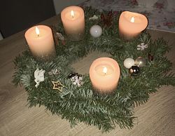 Ein Adventskranz mit Tannengrün und dunkelweißen leuchtenden Kerzen