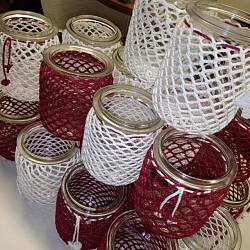 Windlichter, die mit weißen und weinroten Fäden umhäkelt sind, wurden übereinander gestapelt.