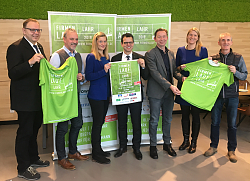 Gruppenbild der Beteiligten des Firmenlaufs, sie halten T-Shirts in die Kamera. 