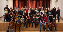 Die Schüler sitzen und stehen mit ihren Instrumenten an der Bühne des Orchestersaal. Mit dabei auch die Lehrkräfte. 