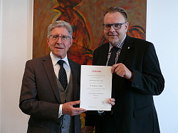 Lahrs erster Bürgermeister Guido Schöneboom überreicht Oberbürgermeister Dr. Wolfgang G. Müller die Urkunde. Beide lächeln in die Kamera. 
